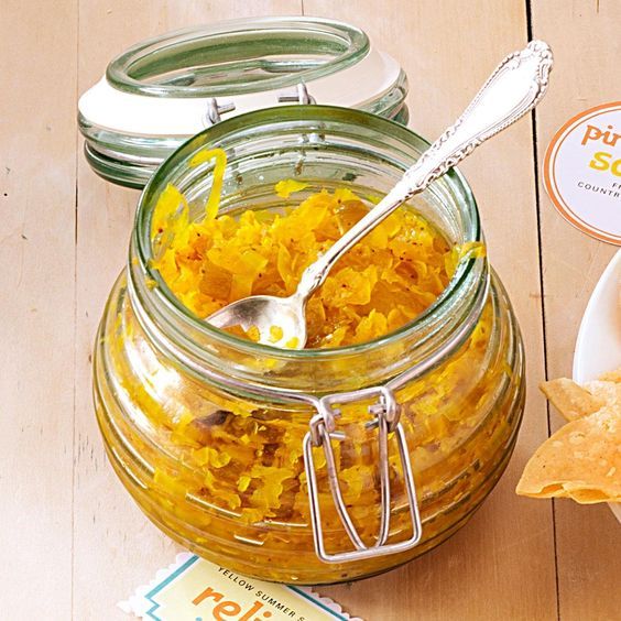 a jar filled with yellow food next to a bowl of tortilla chips and a spoon