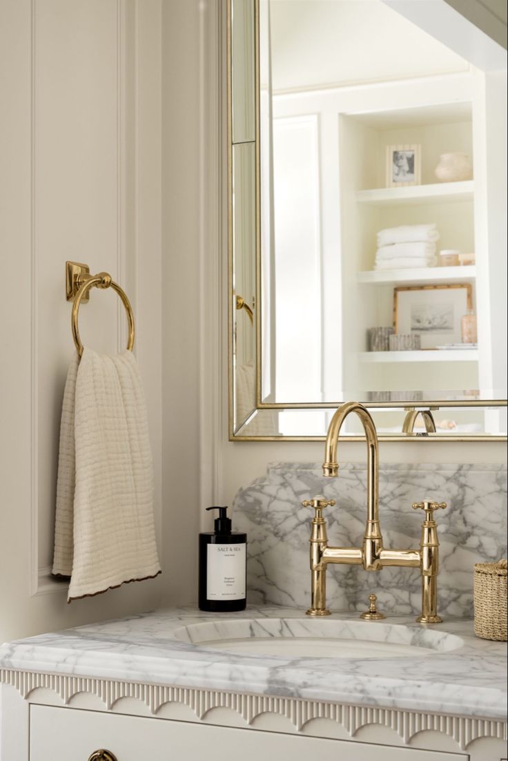 a bathroom with marble counter top and gold faucet, mirror above the sink