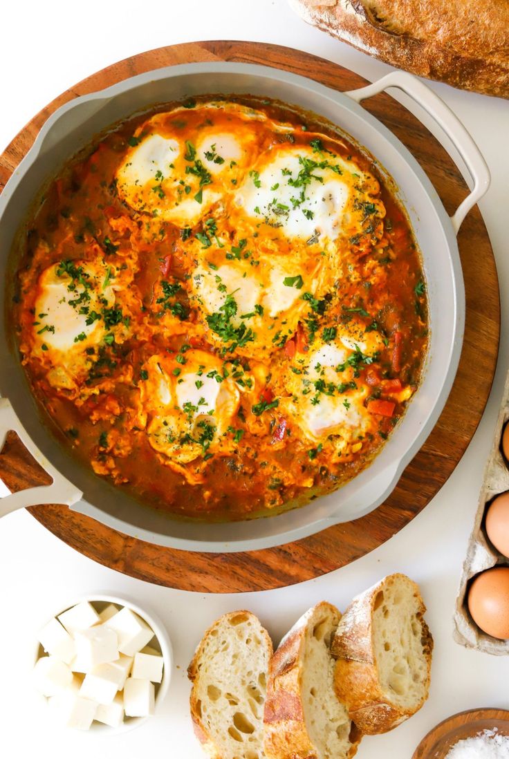 an egg dish in a pan surrounded by bread and other ingredients on a white surface