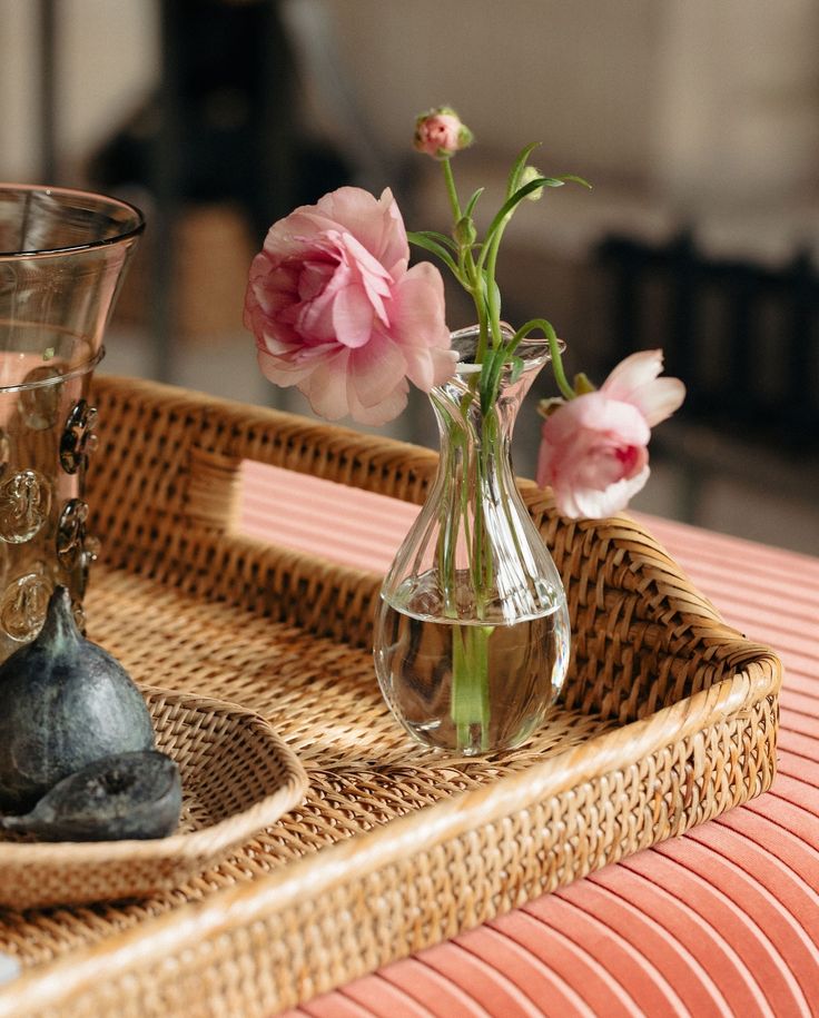 two vases with flowers in them sitting on a wicker tray next to rocks