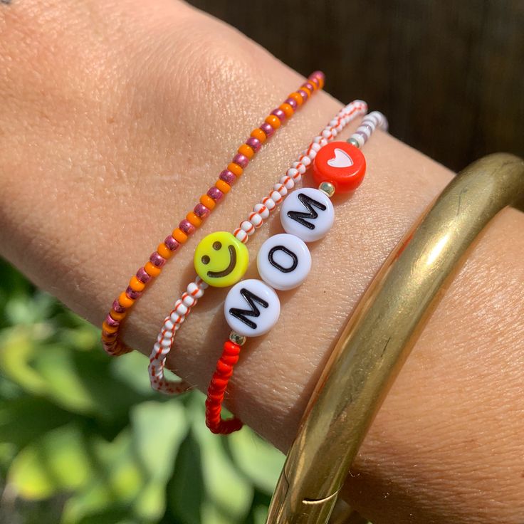 multi colored and patterned seed bead bracelet with MOM, gold beads and a heard bead strung on elastic please gently roll on and off to prolong its life handmade in venice, ca Multicolor Heart Beads Bracelets For Mother's Day, Playful Orange Beaded Bracelets With Letter Beads, Red Adjustable Fun Beaded Bracelets, Playful White Adjustable Beaded Bracelets, Playful Adjustable White Beaded Bracelets, Orange Heishi Beads Jewelry For Friendship, Playful Adjustable White Beaded Bracelet, White Casual Beaded Bracelets For Mother's Day, Casual White Beaded Bracelets For Mother's Day