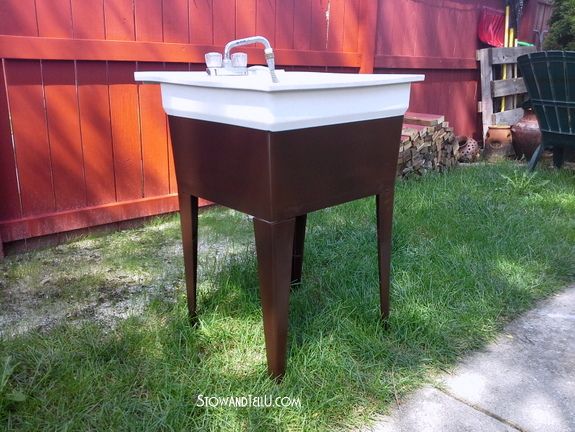 a sink sitting on top of a wooden table in the grass next to a fence