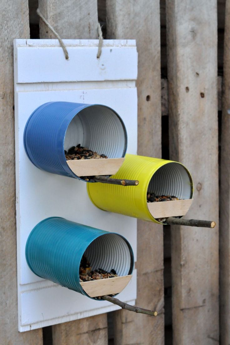 two blue and yellow bird feeders hanging on a wall next to a wooden fence