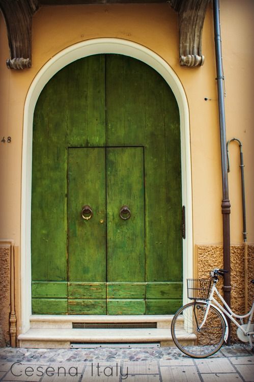 a bicycle parked in front of a green door with arched doorways on the side