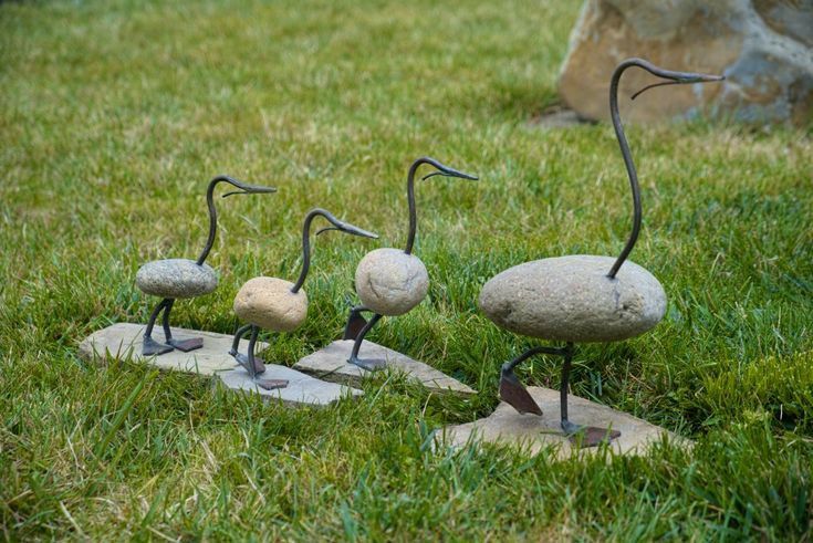 three stone birds sitting on top of each other in the grass next to some rocks