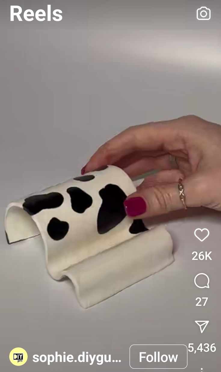 a woman's hand is holding onto a cow napkin holder that has black and white spots on it