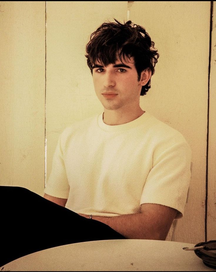 a young man sitting in front of a white wall