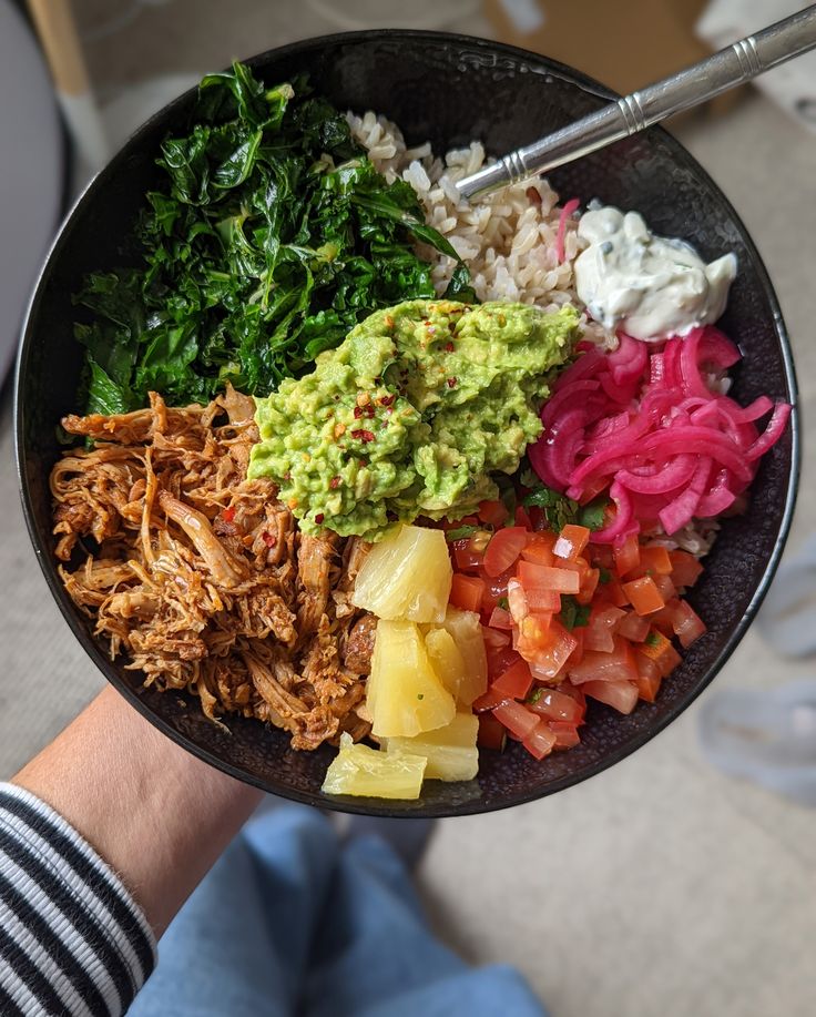 a person holding a bowl filled with different types of food