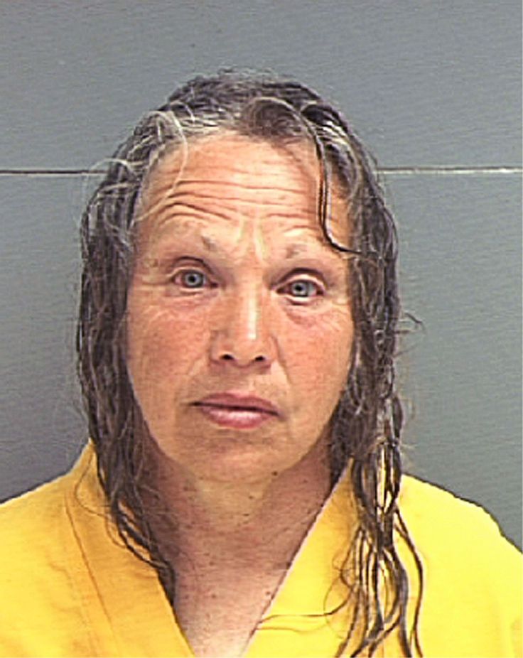 a woman with long hair is mugged in front of a gray wall and wearing a yellow shirt