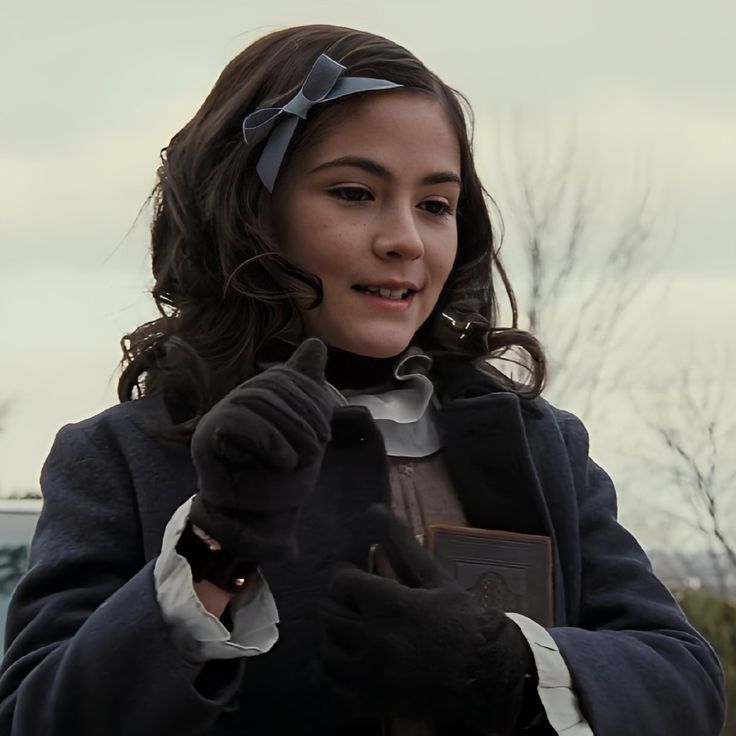 a young woman wearing gloves and holding a book in her right hand while looking at the camera