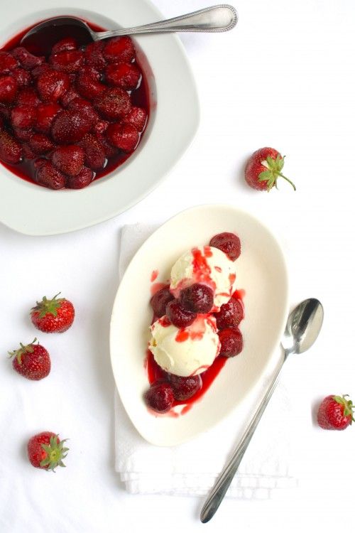 a bowl of ice cream with strawberries on the side and spoon next to it