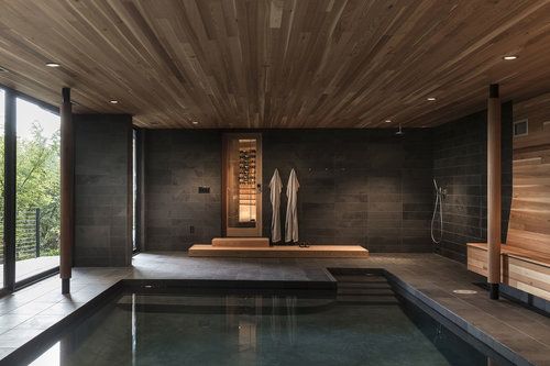 an indoor swimming pool surrounded by wooden walls and flooring, with two saunas on the far wall