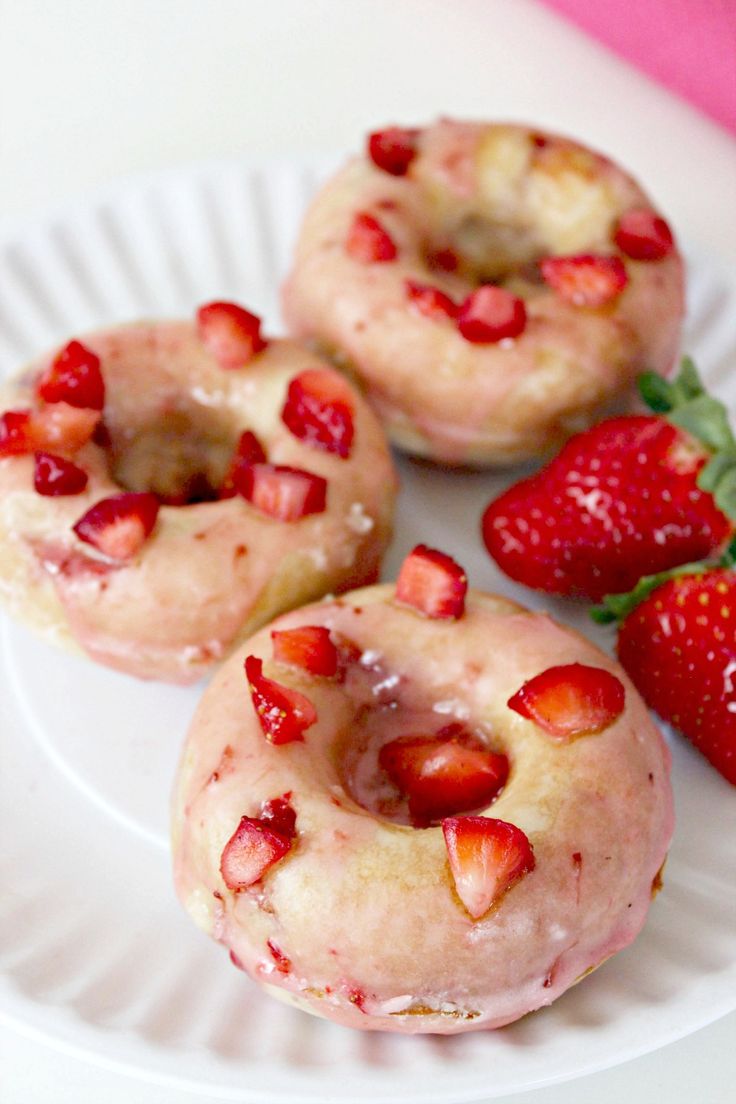 three donuts with strawberry toppings on a white plate next to some strawberries