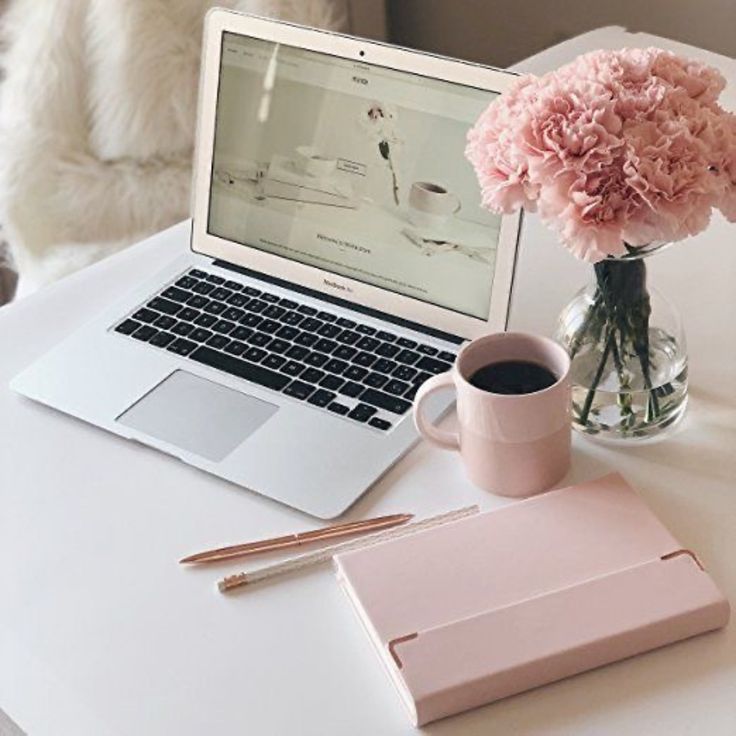 an open laptop computer sitting on top of a white desk next to a vase with pink flowers