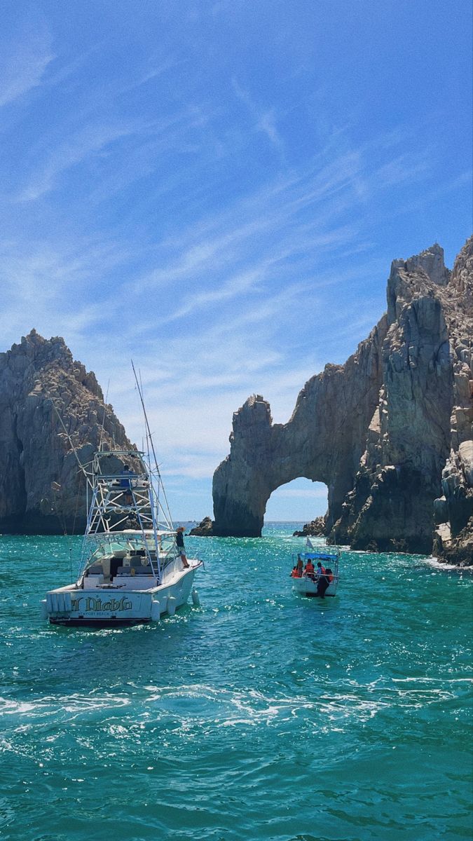 two boats in the water near some rocks and an arch shaped rock outcropping