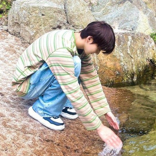 a young boy is playing in the water near rocks and grass, with his hand reaching for something