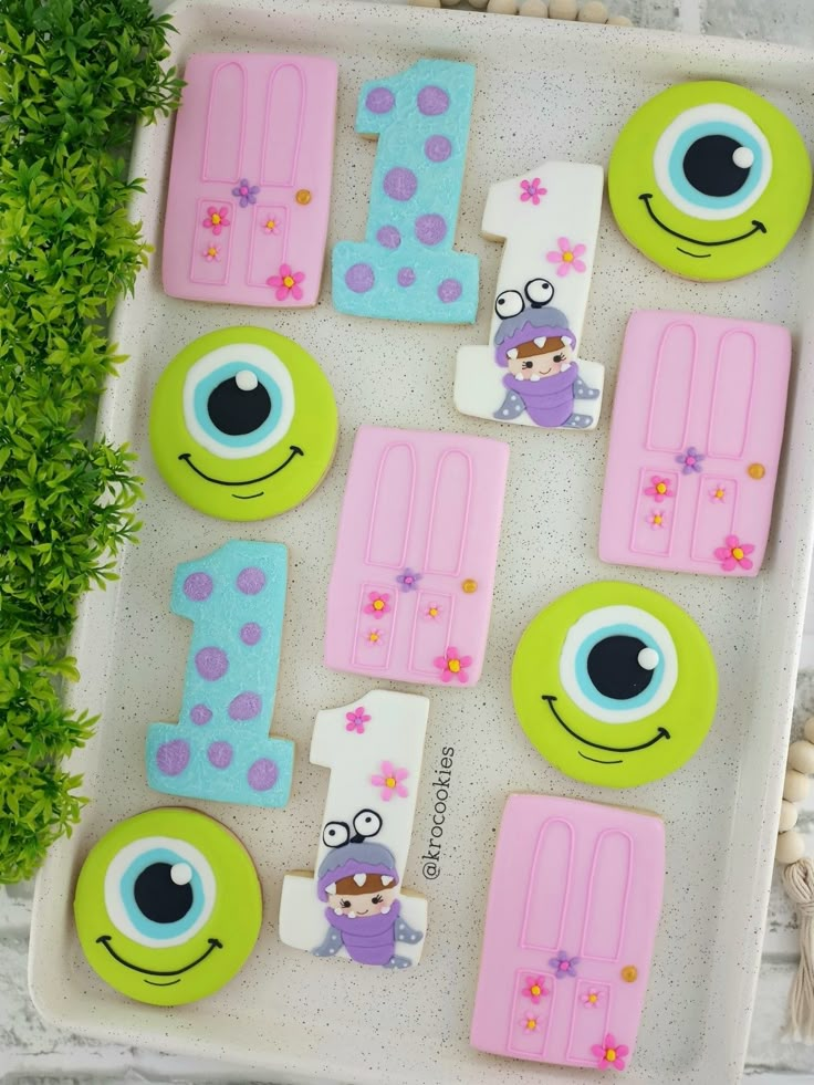 decorated cookies in the shape of numbers and monsters on a tray with plants next to them