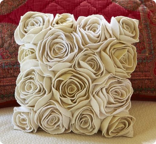 a pillow made out of paper roses on a bed with a red blanket behind it