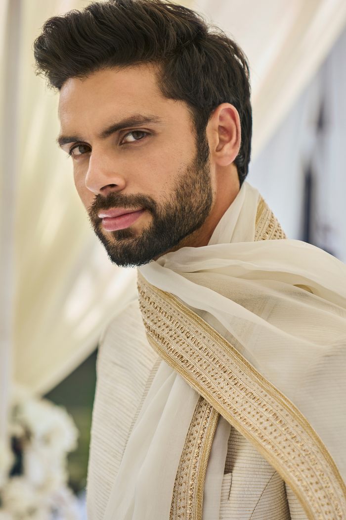 This cream sherwani set features all over gold zari embroidery on a raw silk base. It is paired with a cotton silk kurta and dhoti pants. Completing embroidered stole and footwear is also available.From Seema Gujral's Tuscan Summer collection. DELIVERY TIMEPlease allow 8-12 weeks for your outfit to arrive.FABRIC DETAILSRaw SilkProfessional cleaning only. Gold Dupatta With Naqshi For Diwali, Gold Naqshi Dupatta For Diwali, Naqshi Detailed Dupatta For Traditional Ceremonies And Diwali, Festive Cotton Silk Sherwani With Dupatta, Traditional Gold Unstitched Suit With Naqshi Detailing, Designer Cotton Silk Sherwani With Zari Work, Traditional Gold Unstitched Suit With Naqshi, Traditional Chanderi Sherwani With Dupatta, Chanderi Sherwani With Dupatta For Traditional Ceremonies