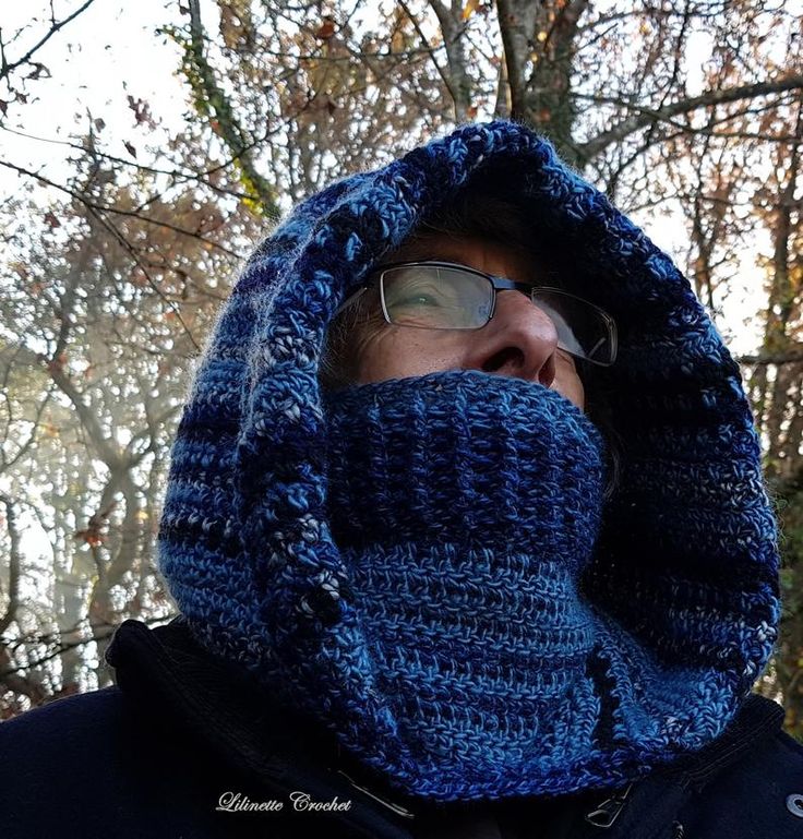 a man wearing a blue knitted hood with his face covered by a scarf in front of some trees