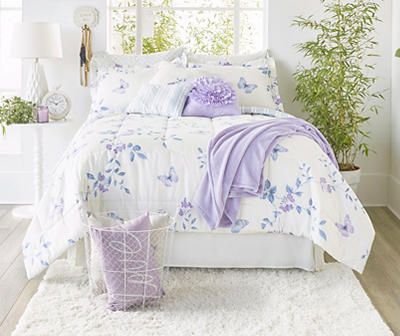 a bed with purple and white comforters in a bedroom next to a plant filled window