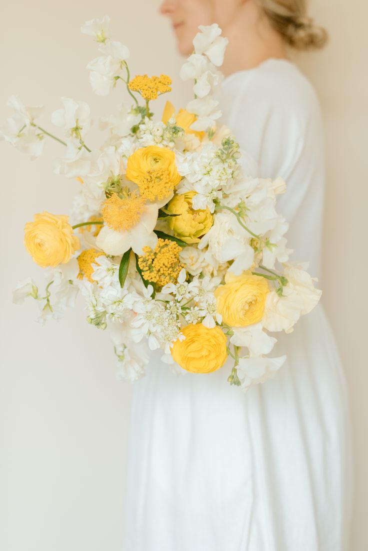 a woman holding a bouquet of yellow and white flowers