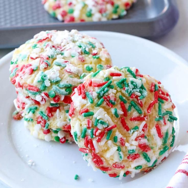 three cookies with sprinkles on a white plate next to a cookie sheet