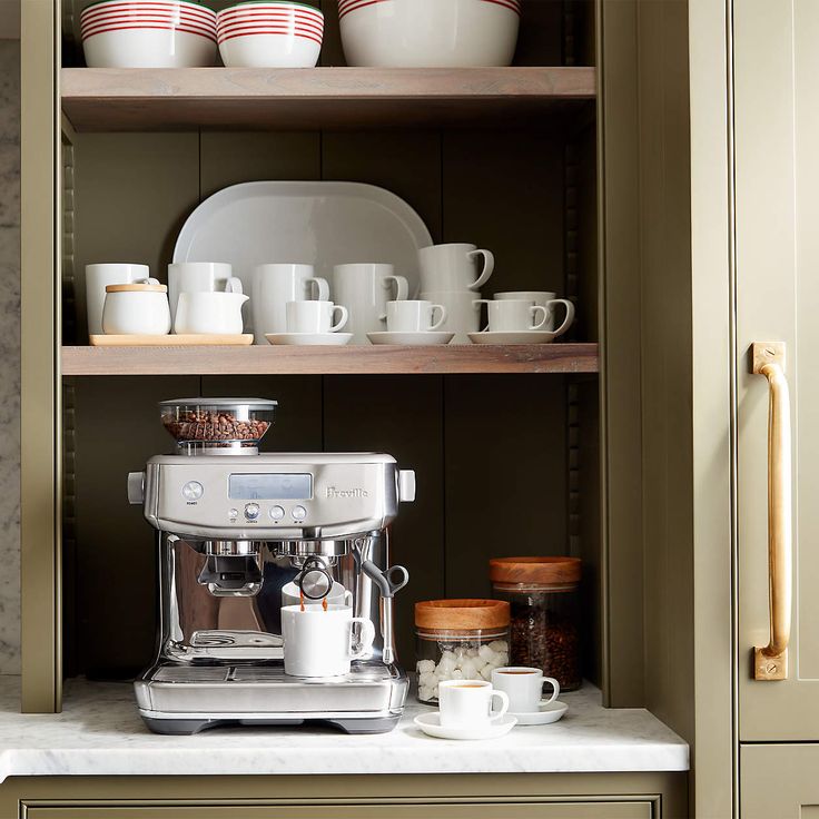 a coffee maker sitting on top of a counter next to cups and saucers in a kitchen