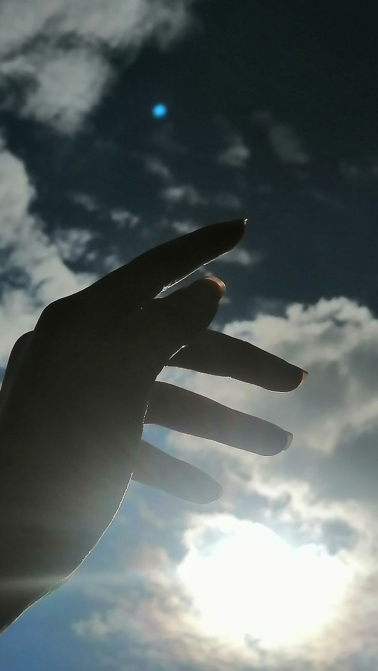 a person's hand reaching up into the air with clouds in the sky behind them