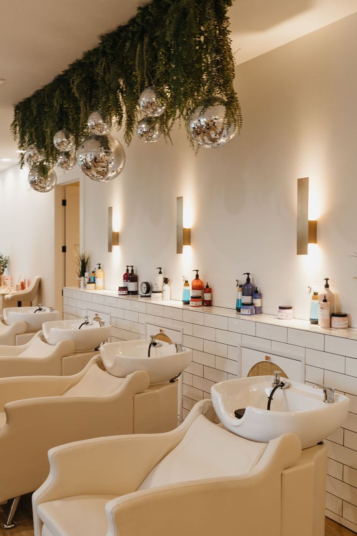 the interior of a hair salon with white chairs and hanging ornaments on the wall above them