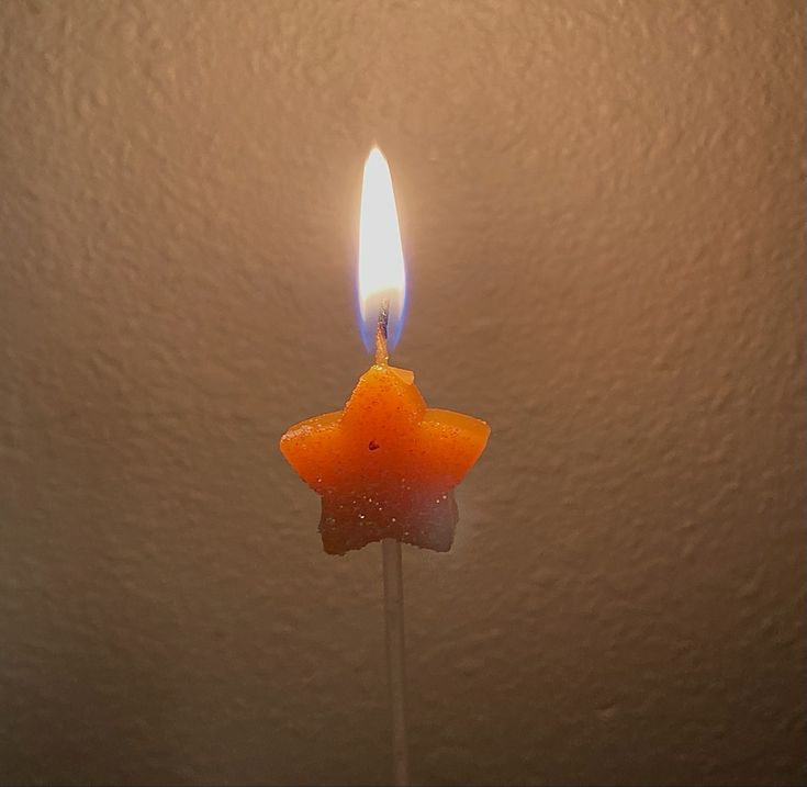 an orange candle with a star on it sitting in the middle of a room next to a wall