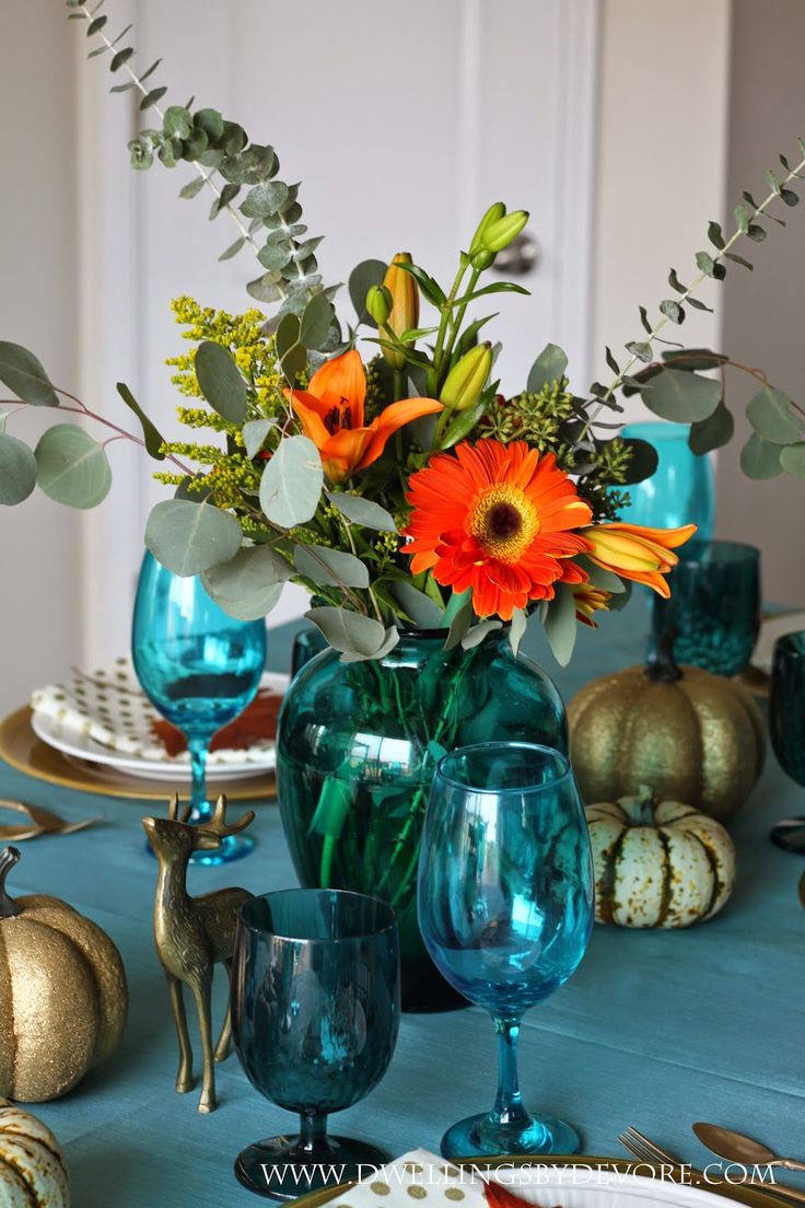 a table topped with blue glass vases filled with flowers and greenery next to pumpkins