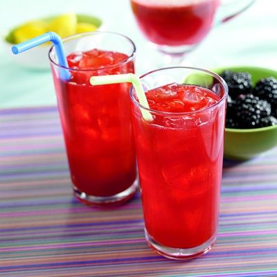 two glasses filled with red drinks sitting on top of a table next to bowls of fruit