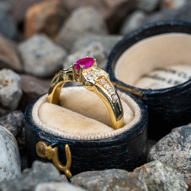 an engagement ring with a red stone in it sits on rocks next to another ring