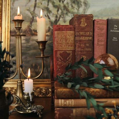 candles and books on a table in front of a painting