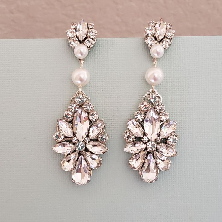 a pair of earrings with pearls and crystal stones on top of a gray surface next to a pink wall