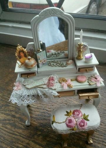 a dollhouse desk with a mirror and pink roses on it's top, sitting next to a window