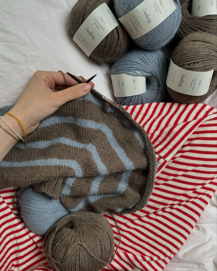 a person is knitting on a blanket with balls of yarn next to it and two crochet hooks