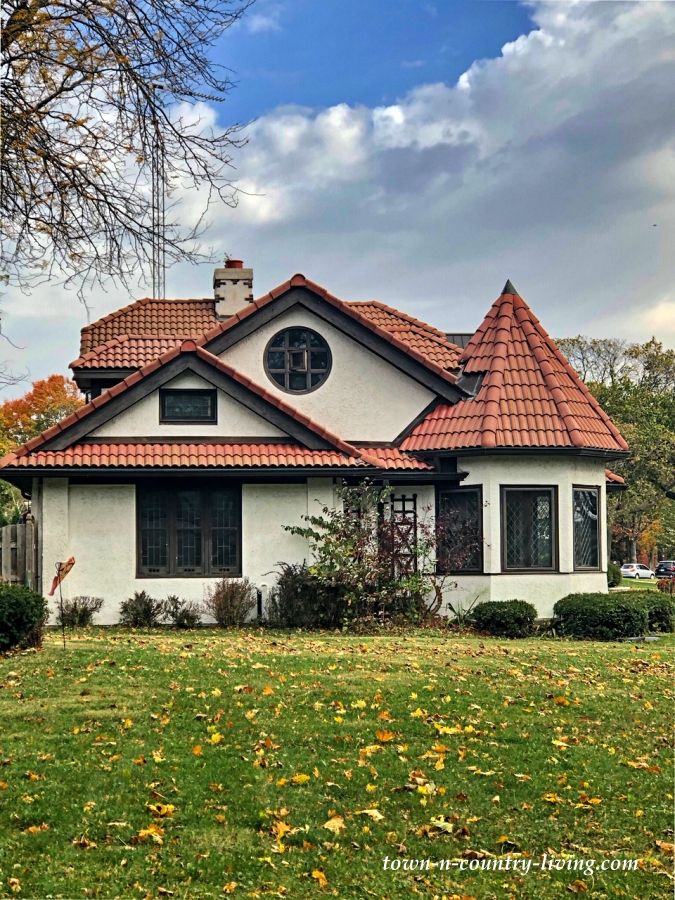 a white house with a red roof surrounded by green grass and autumn leaves on the ground