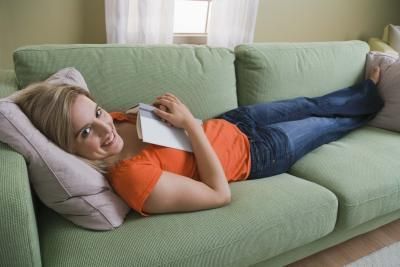 a woman laying on top of a green couch next to a window reading a book