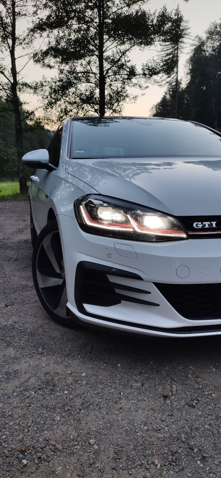 the front end of a white car parked on gravel