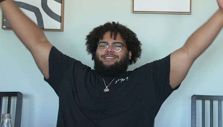 a man with curly hair and glasses holding his arms in the air