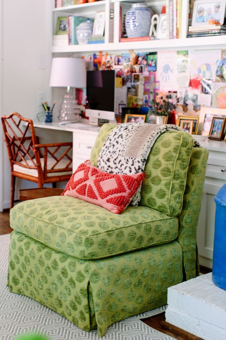 a green chair sitting in a living room next to a white desk and book shelf