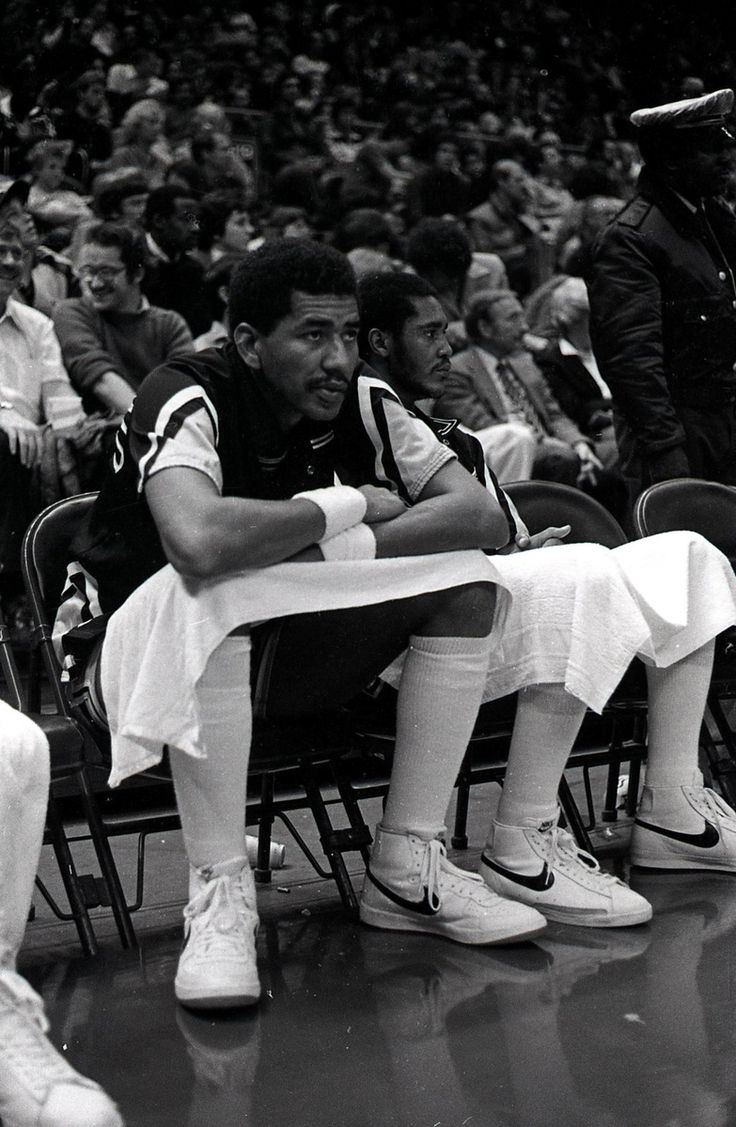 a black and white photo of a man sitting on a bench in front of a crowd