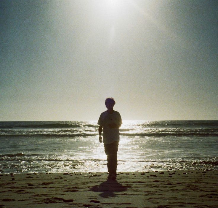 a man standing on top of a beach next to the ocean under a blue sky