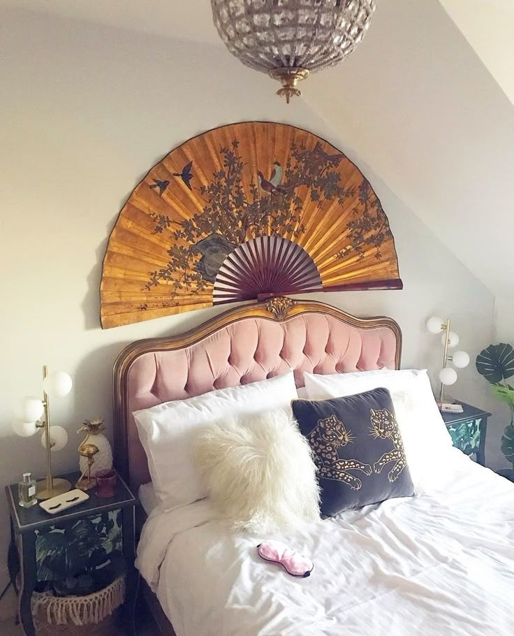 a bed with white sheets, pillows and a fan on the wall above it's headboard