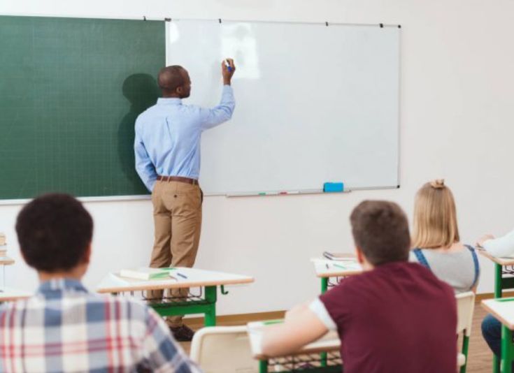 a man is writing on a whiteboard in front of his class while others watch