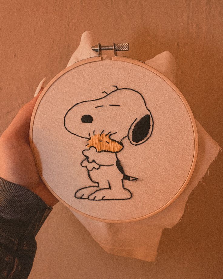 a person holding up a cross stitch embroidery with a cartoon character on it's face