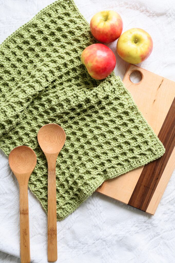 a crocheted dish towel with wooden spoons and apples