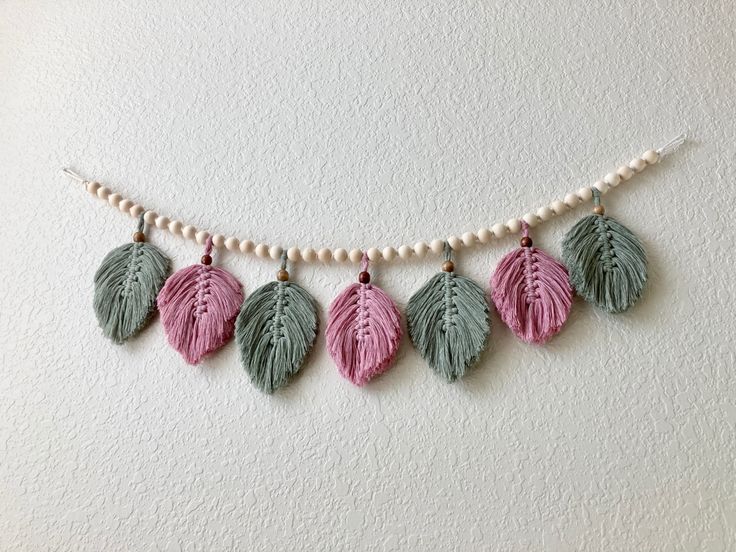 a necklace with pink and green leaves hanging from it's side on a white wall